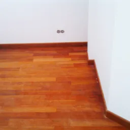 Nowo ułożony, lakierowany parkiet drewniany z ozdobną listwą przypodłogową, widoczne gniazdka elektryczne w ścianie.