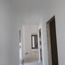 Korytarz w trakcie malowania na biało, widoczne niedokończone obramowania drzwi, puszka z farbą Rapid na podłodze.