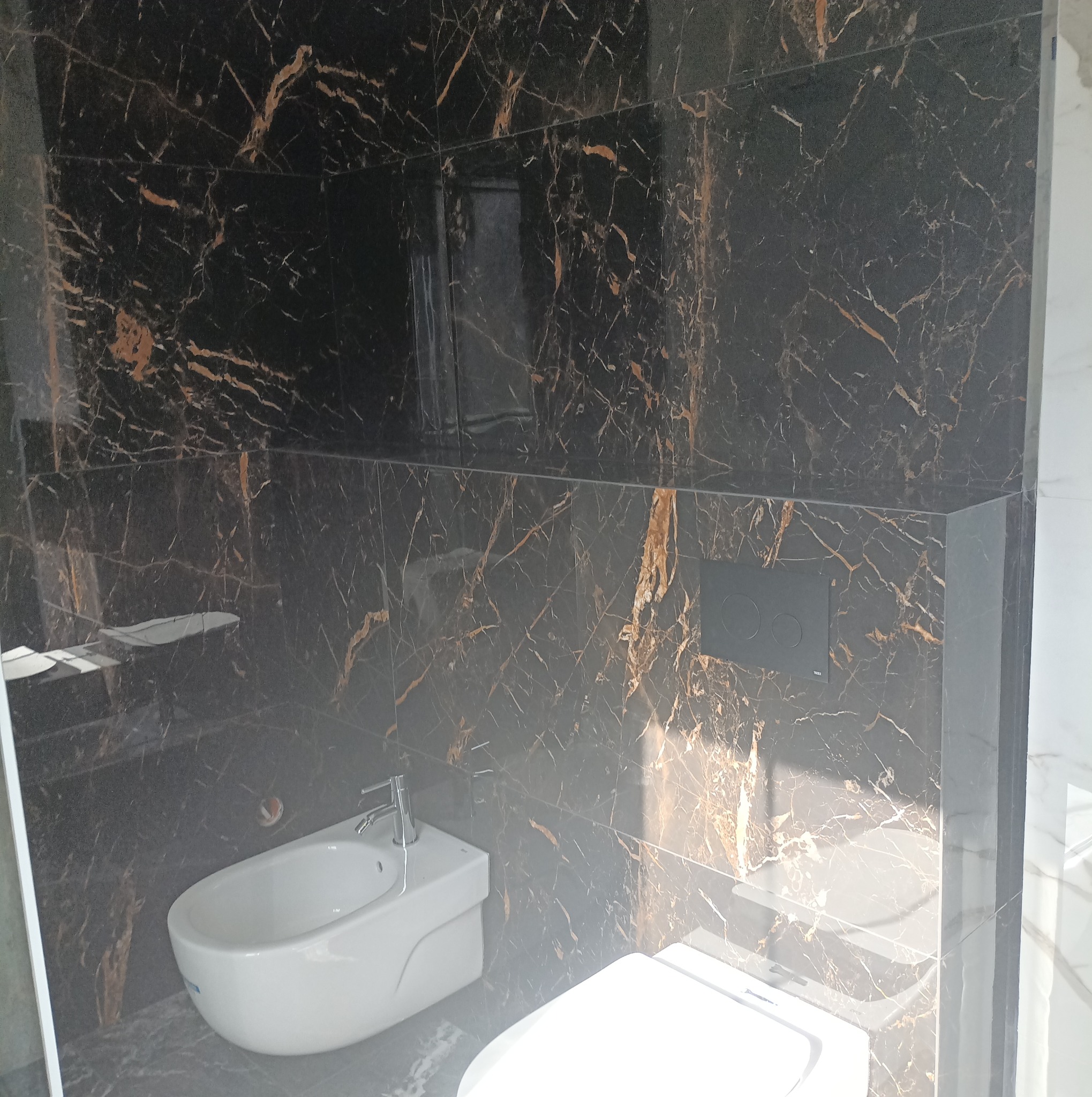 Nowoczesna łazienka w Zielonej Górze z czarnymi płytkami imitującymi marmur ze złotymi żyłami, wyposażona w biały bidet i toaletę.