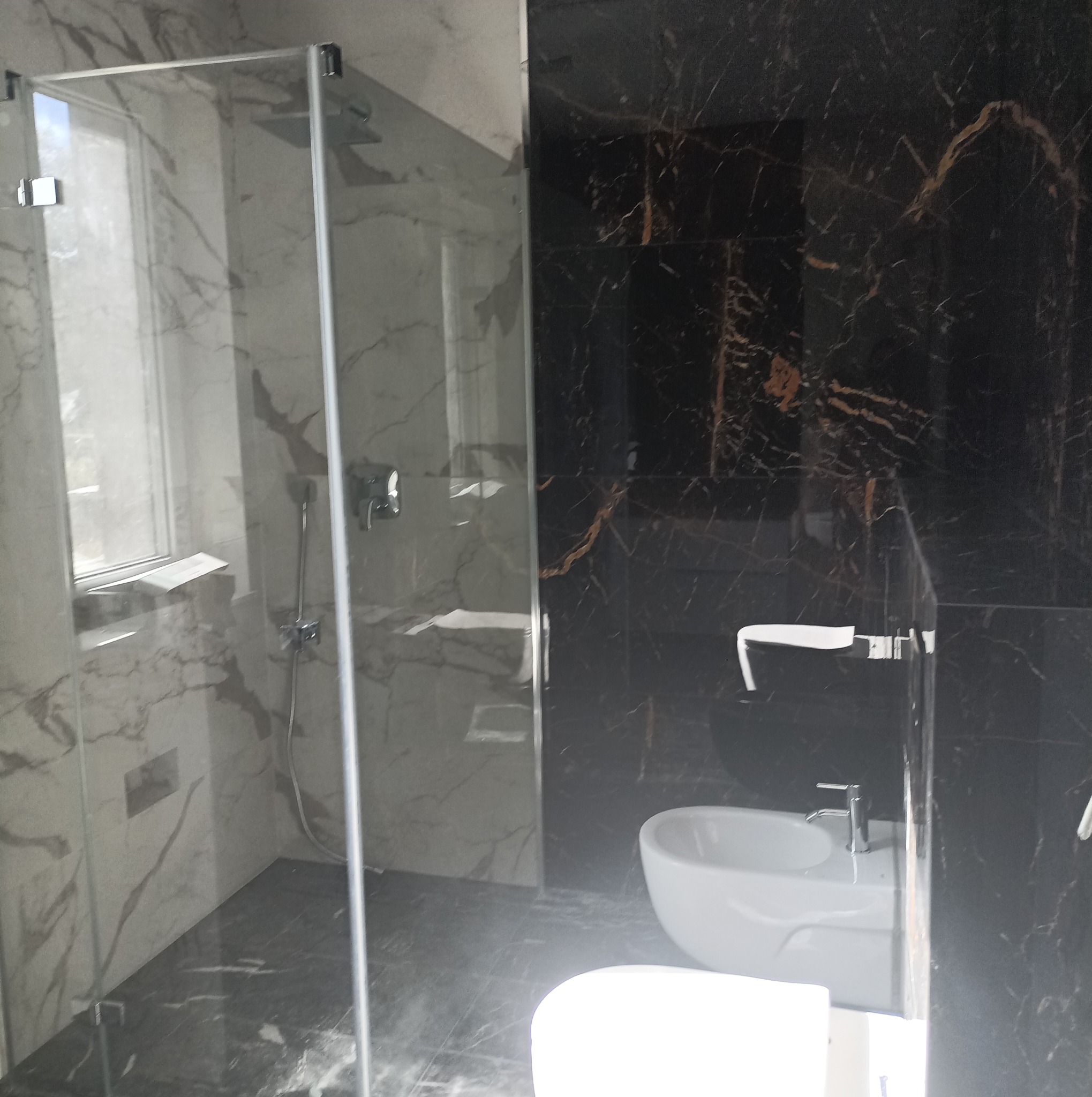 Nowoczesna łazienka z kabiną prysznicową typu walk-in, białą umywalką i czarnymi płytkami imitującymi marmur z złotymi żyłami.