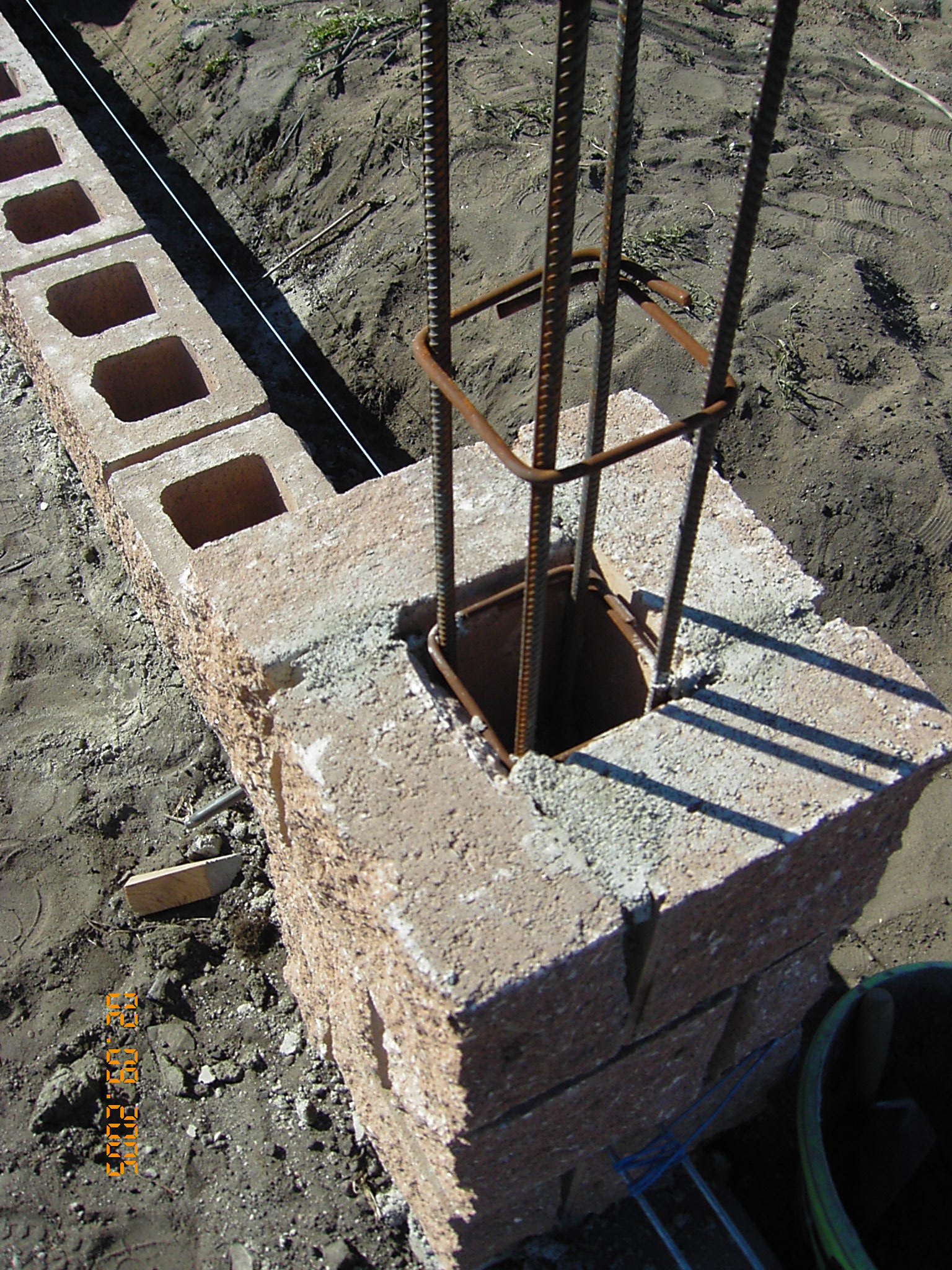 Wznoszenie ścian fundamentowych z bloczków betonowych z wkładką zbrojeniową, widoczna lina wyznaczająca prostą linię fundamentu.