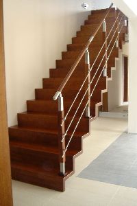 Wewnętrzne schody z ciemnego drewna z prostymi, pionowymi balustradami ze stali nierdzewnej, widok z dołu, jasne wnętrze.