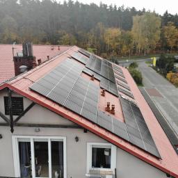 Szymel-bud - Widok z góry na dom z czerwonym dachem, na którym zamontowane są panele słoneczne; w tle widoczna droga i drzewa w jesiennych kolorach.