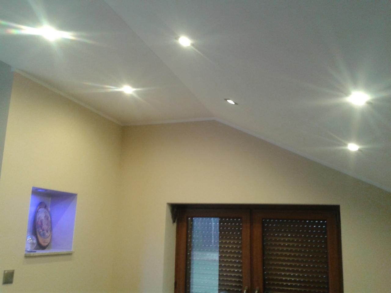 Jasne wnętrze z oświetleniem punktowym w suficie skośnym, drewniane drzwi balkonowe i wnęka z dekoracją, kremowe ściany.