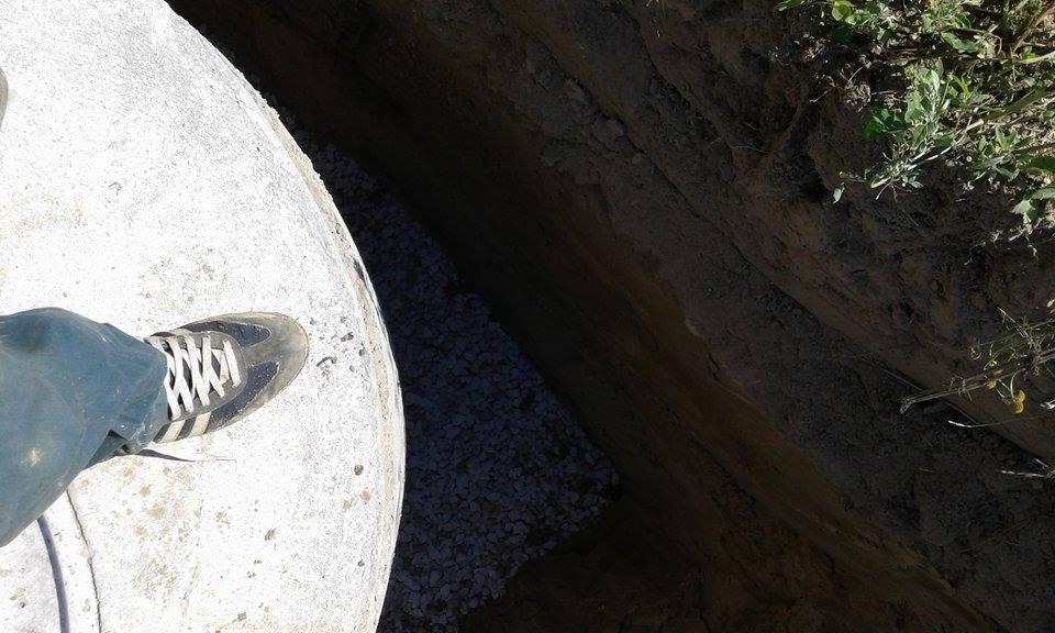 Stopa w sportowym bucie na betonowej pokrywie szamba w wykopie z podsypką żwirową.