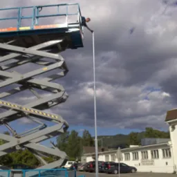 Montaż pionowego uziomu instalacji odgromowej we Wrocławiu z wykorzystaniem podnośnika nożycowego, widoczne budynki w tle.