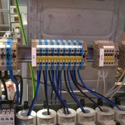 Artel Electric - Szyna z zamontowanymi listwami zaciskowymi oznaczonymi X0, X1, X10, X11, X12, z podłączonymi przewodami w kolorze niebieskim i czarnym.