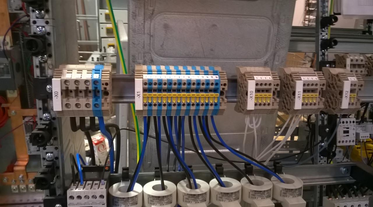 Szyna z zamontowanymi listwami zaciskowymi oznaczonymi X0, X1, X10, X11, X12, z podłączonymi przewodami w kolorze niebieskim i czarnym.