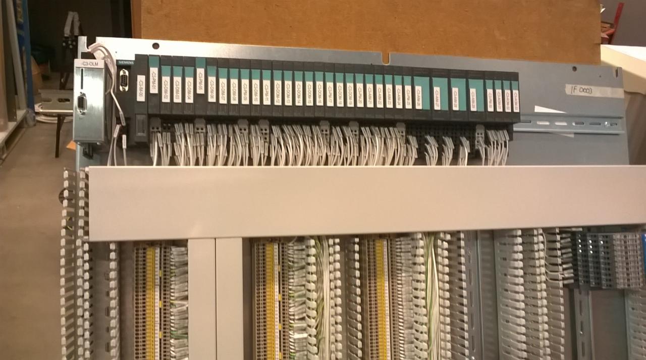 Rozbudowana szafa sterownicza z modułami Siemens, okablowaniem i listwami zaciskowymi, widoczne etykiety opisujące poszczególne moduły.