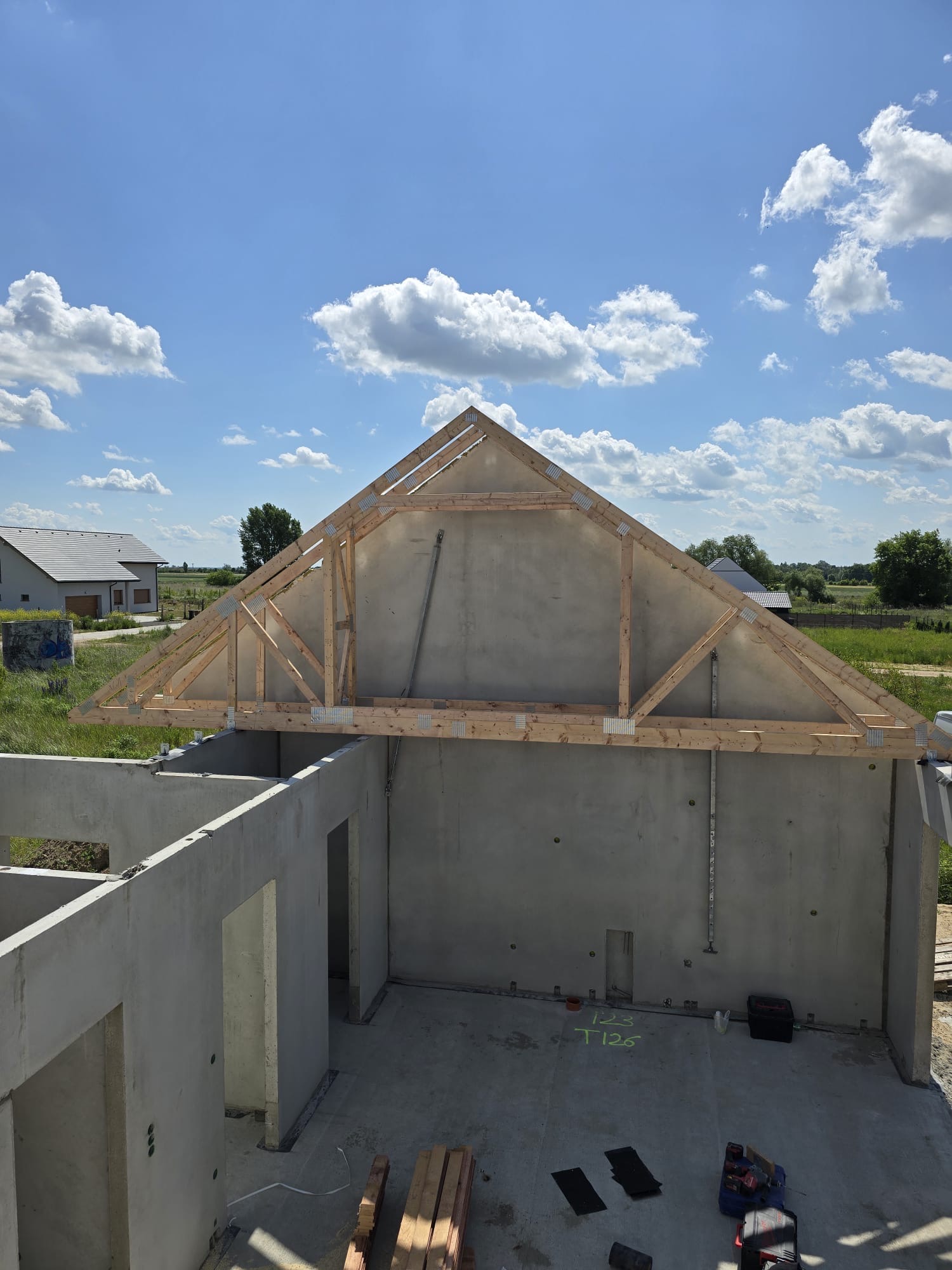 Surowy stan domu z betonu komórkowego z drewnianą konstrukcją dachu w trakcie budowy, widok z góry na tle błękitnego nieba z chmurami.