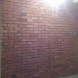 Ściana wykończona cegłą dekoracyjną wewnątrz pomieszczenia, widoczny fragment otworu drzwiowego i fragment pomalowanej na biało ściany, oświetlenie górne.