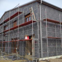 PHU COMPLEX GRZEGORZ ZIMNIAK - Dom w trakcie ocieplania elewacji styropianem grafitowym, widoczne rusztowania i resztki materiału na ziemi.