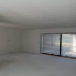 Wnętrze w stanie deweloperskim z przygotowanymi ścianami pod malowanie, okno zabezpieczone folią ochronną, widoczne przewody elektryczne.