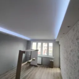 Wykończone wnętrze w Szczecinie z podwieszanym sufitem z oświetleniem LED, dekoracyjną ścianą z imitacji kamienia i drewnianą konstrukcją w trakcie montażu.