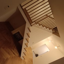 Stolarstwo Marszałek Przemysław - Nowoczesne schody z drewnianymi stopniami i ażurową konstrukcją, widziane z góry, z parkietem w jodełkę i oświetleniem punktowym w tle.