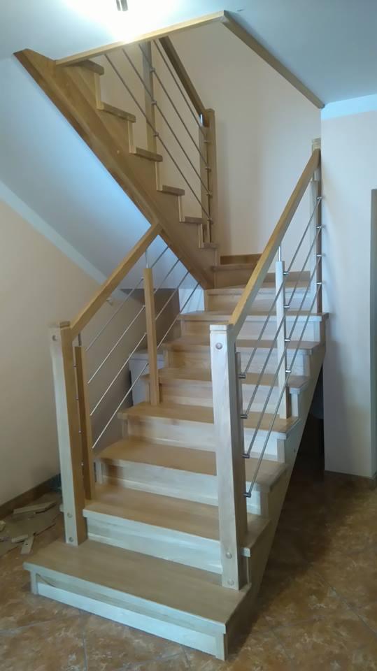 Jasne drewniane schody z metalowymi balustradami w nowoczesnym domu, widoczne elementy montażowe i listwy przypodłogowe.