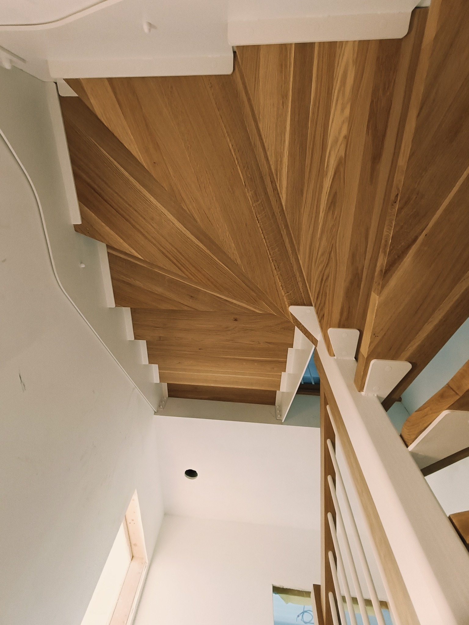 Nowoczesne schody z drewna dębowego, widok z dołu, z białymi wspornikami i balustradą. Minimalistyczny design, jasne wnętrze, naturalne światło.