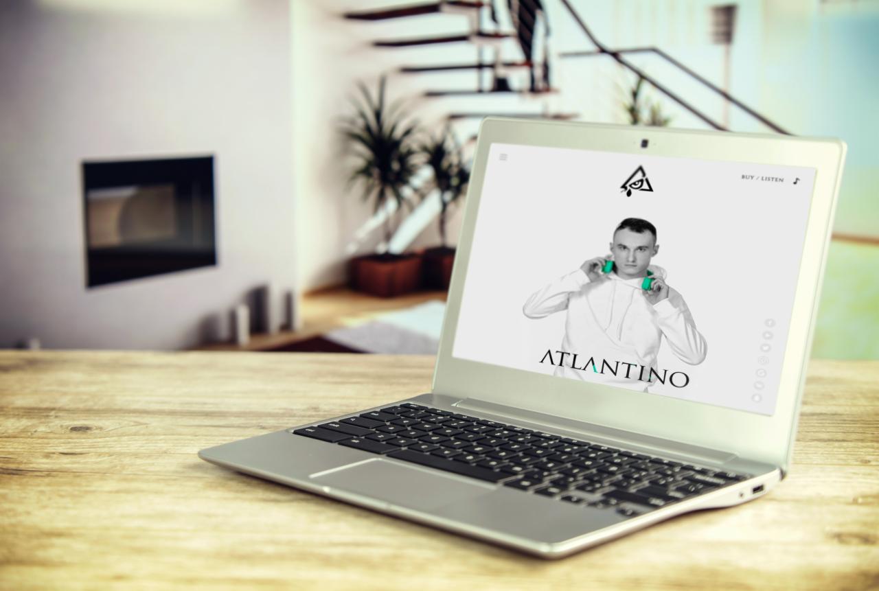 Laptop na drewnianym stole wyświetla stronę internetową artysty muzycznego z jego zdjęciem w słuchawkach i logo.