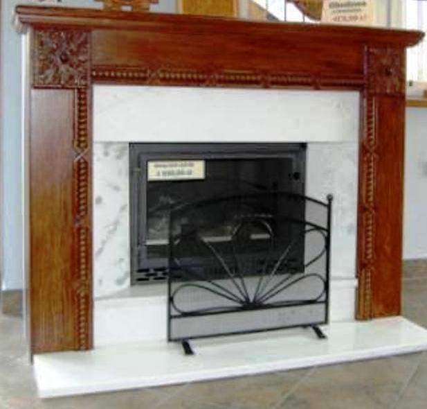 Portal kominkowy z litego drewna o ciemnym odcieniu, z delikatnymi zdobieniami, otaczający wkład kominkowy z czarną kratą ochronną.