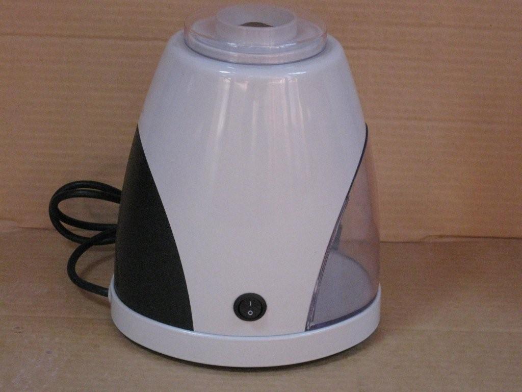 Kompaktowa, biała kruszarka do lodu z czarnymi i przezroczystymi elementami, widoczny przewód zasilający i włącznik, ustawiona na brązowym tle.