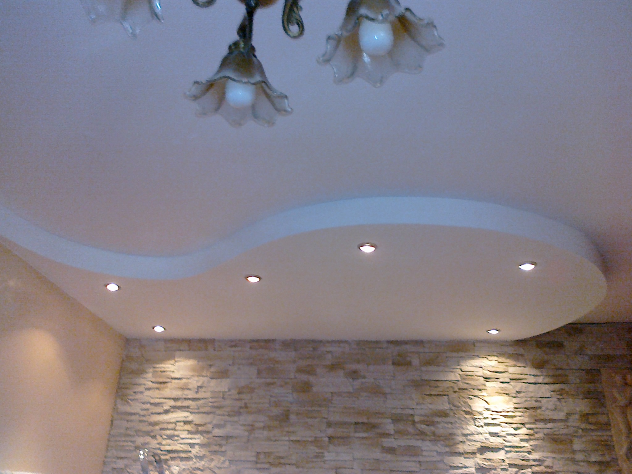 Falisty podwieszany sufit z oświetleniem punktowym, wisząca lampa w stylu retro i ściana z kamienia dekoracyjnego.