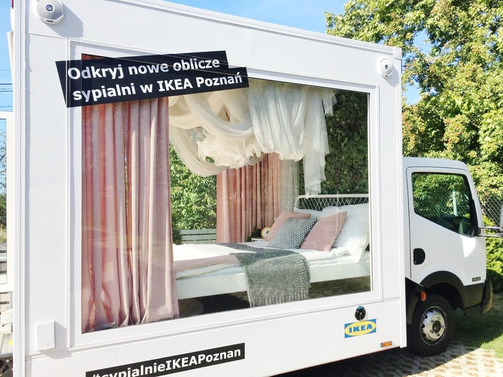 Mobilna ekspozycja sypialni IKEA Poznań wewnątrz białej ciężarówki z dużym oknem, z plakatem reklamowym i hashtagiem #sypialnieIKEAPoznan.