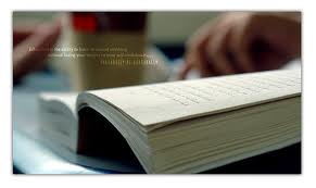 Otwarta książka leżąca na stole, z widocznymi palcami osoby przeglądającej strony. Tekst na stronie jest rozmazany, a tło jest delikatnie rozmyte, tworząc spokojną atmosferę.