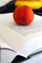 Otwarta książka leżąca na stole z brzoskwinią na stronie, w tle widoczny banan.