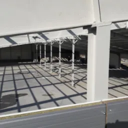 Wnętrze nowo wznoszonej hali stalowej z widoczną konstrukcją nośną, betonową posadzką i częściowo zamontowaną obudową ścian zewnętrznych z paneli warstwowych.