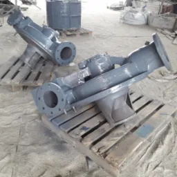 Dwa elementy metalowe w szarym kolorze, prawdopodobnie pompy, leżące na paletach w hali produkcyjnej, po zakończonym procesie obróbki.