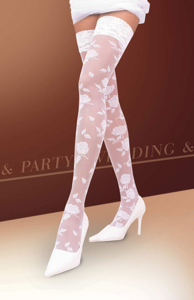 Nogi modelki w białych, transparentnych rajstopach z kwiatowym wzorem i koronkowym wykończeniem, w białych szpilkach na tle brązowo-beżowym.