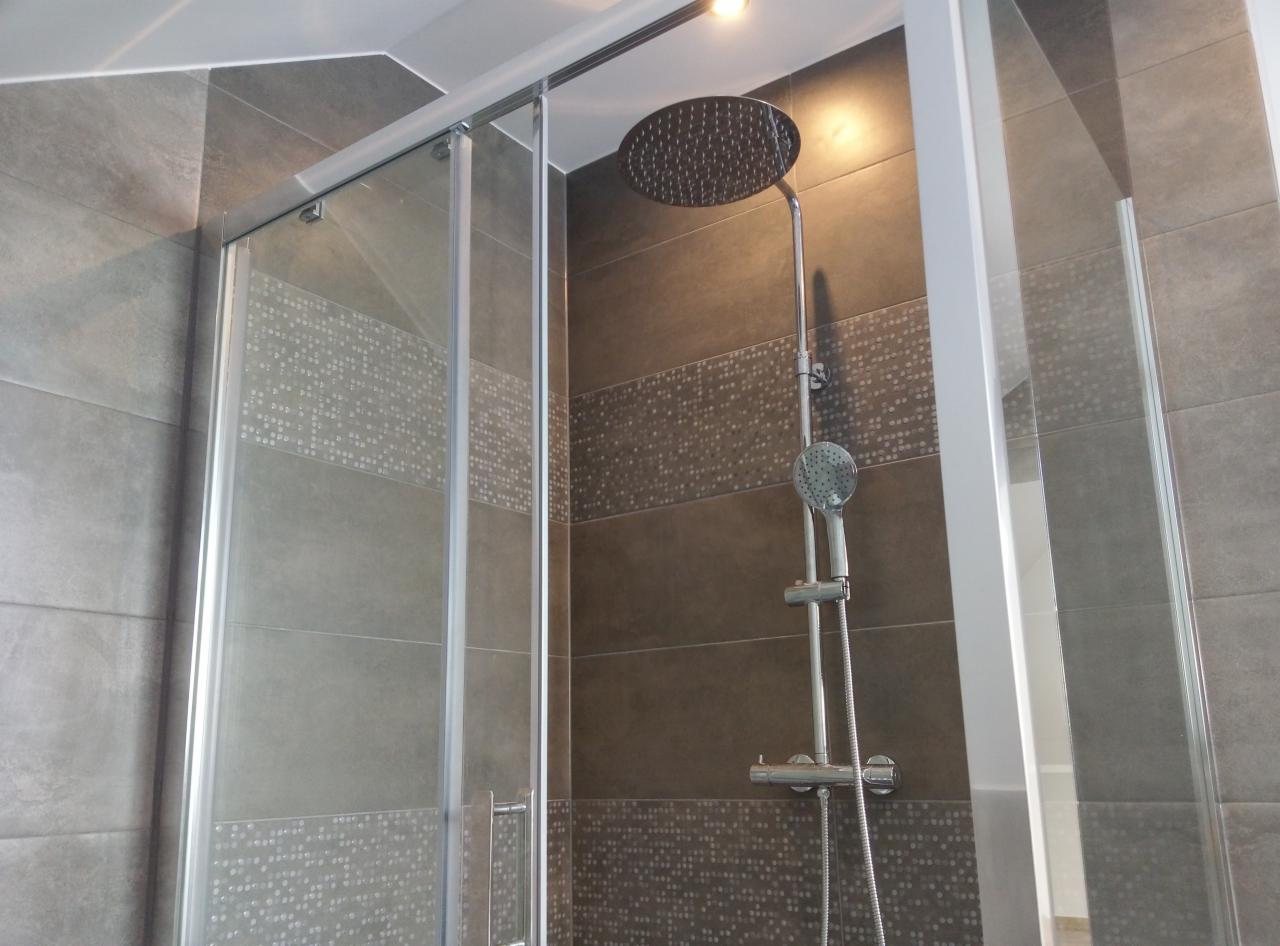 Nowoczesna kabina prysznicowa z przesuwnymi drzwiami, wykończona szarymi płytkami z dekoracyjnym pasem z mozaiki, deszczownica zamontowana na ścianie.