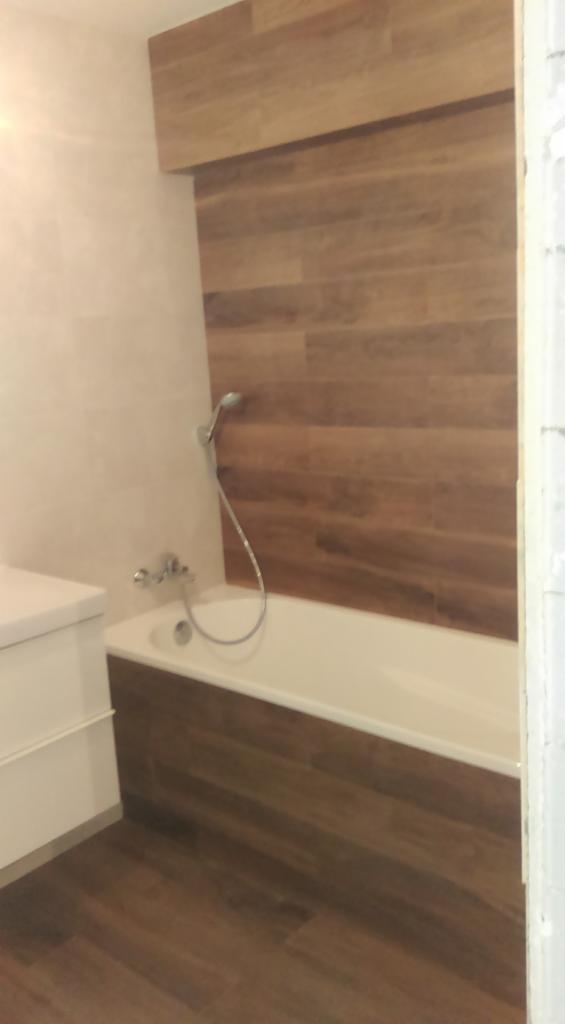 Wykończona łazienka z wanną obudowaną panelami imitującymi drewno i ścianą nad wanną wyłożoną panelami drewnopodobnymi w poziomym układzie.