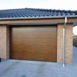 Brązowa segmentowa brama garażowa z poziomymi panelami, zamontowana w garażu z ceglanymi filarami, widoczny system odprowadzania wody deszczowej.