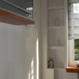 Ściana z zamontowanymi płytami gipsowo-kartonowymi, tworzącymi wnęki dekoracyjne, oświetlona naturalnym światłem wpadającym przez okno z roletą rzymską.