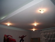 Biały sufit podwieszany z płyt gipsowo-kartonowych z zamontowanymi punktowymi lampami halogenowymi, w pokoju dziecięcym z widocznymi postaciami z bajek na ścianie.