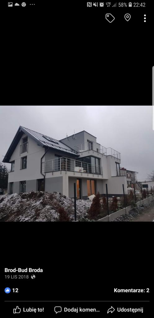 Nowoczesny dom z balkonami w Niedźwiedziu, z częściowo wykonaną elewacją w kolorze szarym, otoczony niewielkim ogrodem i resztkami śniegu.