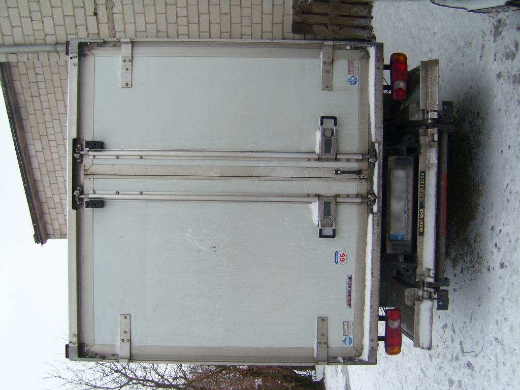 Zamknięte, dwuskrzydłowe drzwi chłodni-mroźni zamontowane na samochodzie dostawczym, widoczne od tyłu na tle zimowego krajobrazu.