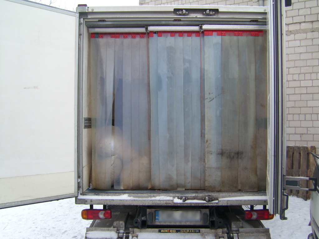 Otwarta przestrzeń ładunkowa chłodni samochodowej z kurtyną paskową z tworzywa sztucznego, widoczne tablice rejestracyjne pojazdu na tle śniegu.