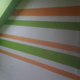 Pokój na poddaszu po malowaniu ścian w poziome pasy: zielone, pomarańczowe i białe. Widoczny grzejnik i okno dachowe.