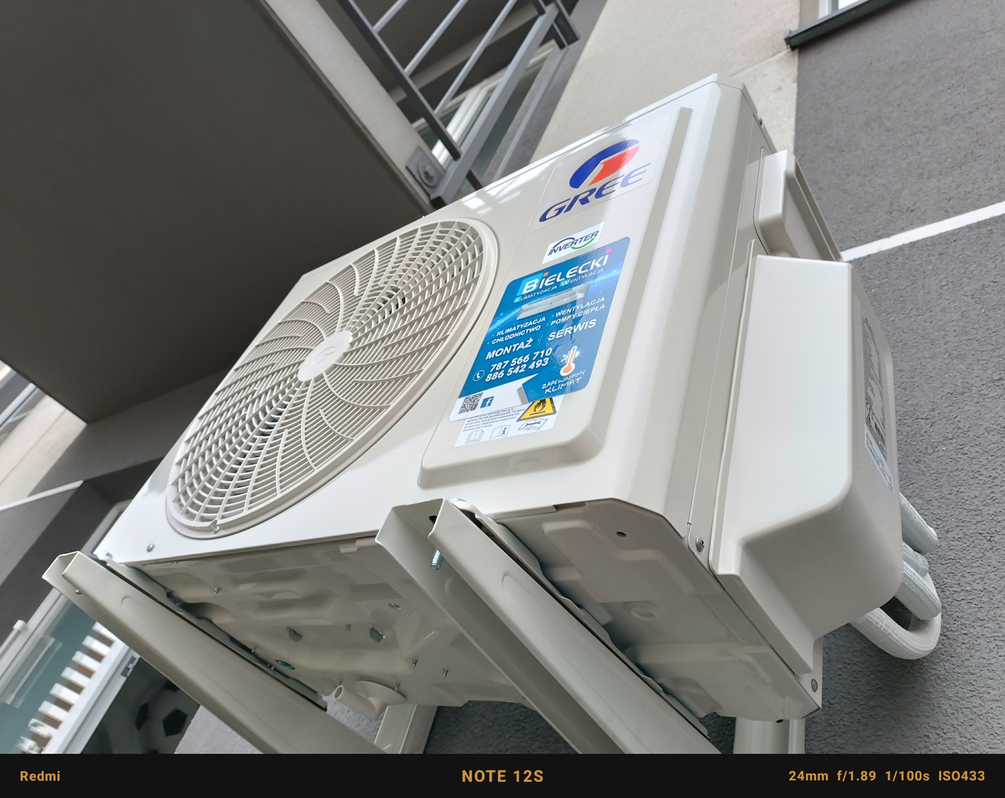 Zewnętrzna jednostka klimatyzacji marki Gree zamontowana na ścianie budynku z widoczną naklejką firmy Bielecki oferującej montaż i serwis klimatyzacji, wentylacji i pomp ciepła.