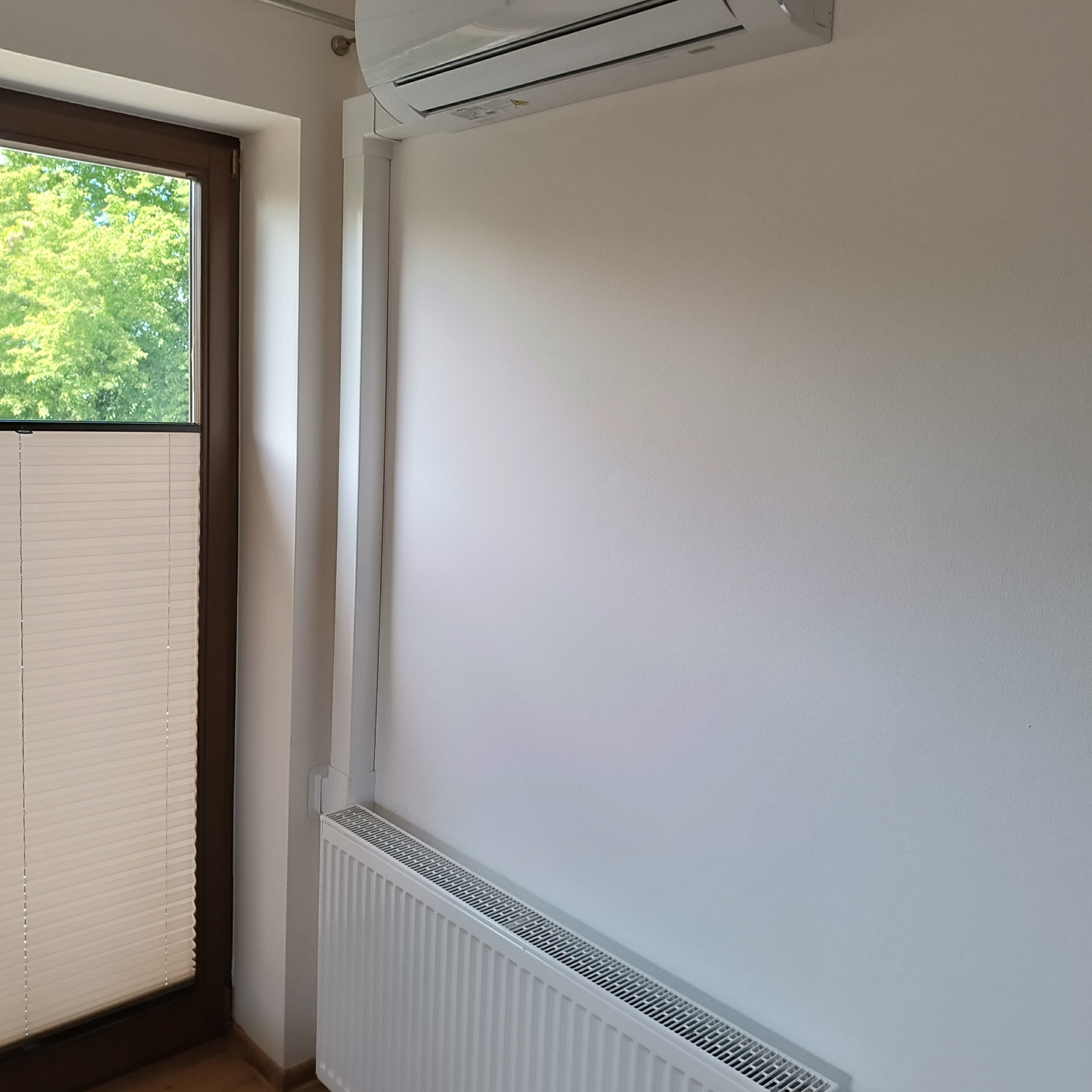 Zamontowana klimatyzacja w domu w Proszowicach, z widocznym białym panelem ściennym i grzejnikiem pod spodem, obok okna z żaluzjami.