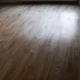 Ułożony parkiet drewniany z widocznym usłojeniem i delikatnym połyskiem, oświetlony naturalnym światłem wpadającym z okna, w tle ściana z grzejnikiem.