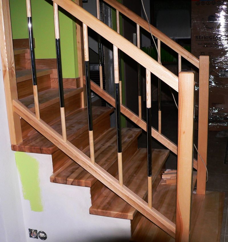 Nowe, drewniane schody z balustradą z elementami metalowymi, częściowo pomalowaną ścianą i widocznymi gniazdkami elektrycznymi.