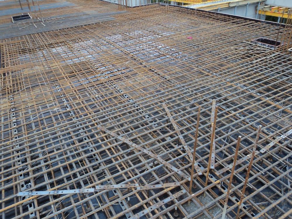 Siatka zbrojeniowa na budowie, widok z góry na rozległą konstrukcję stalową przygotowaną do zalania betonem, z elementami szalunku w tle.