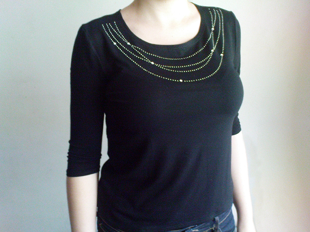 Czarna bluzka z dzianiny z rękawem 3/4 i aplikacją z drobnych, srebrnych dżetów ułożonych w kaskadowe linie wokół dekoltu.