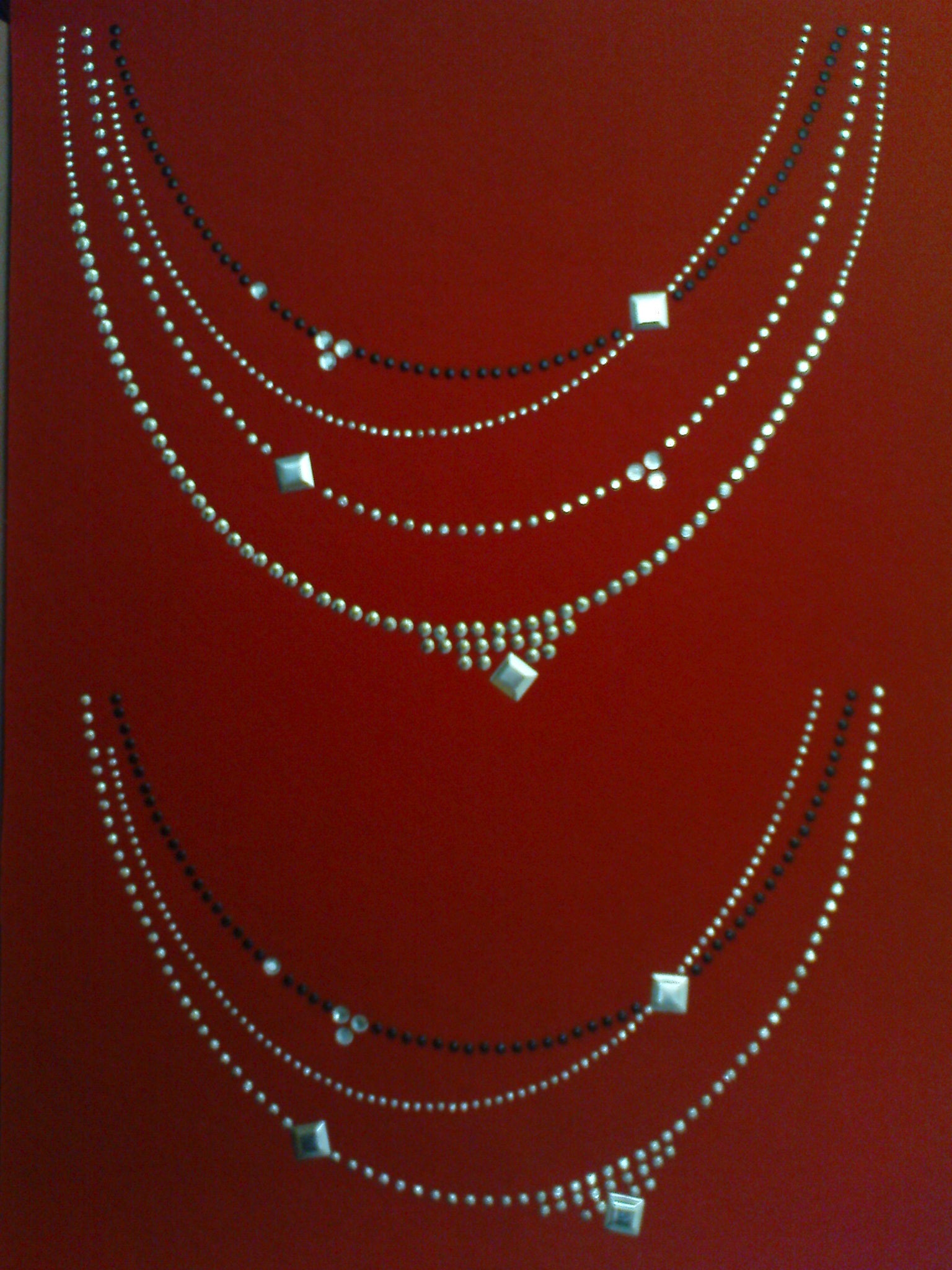 Dwa wzory aplikacji z dżetów i koralików w kształcie naszyjników na czerwonym tle, jeden wzór ułożony nad drugim.