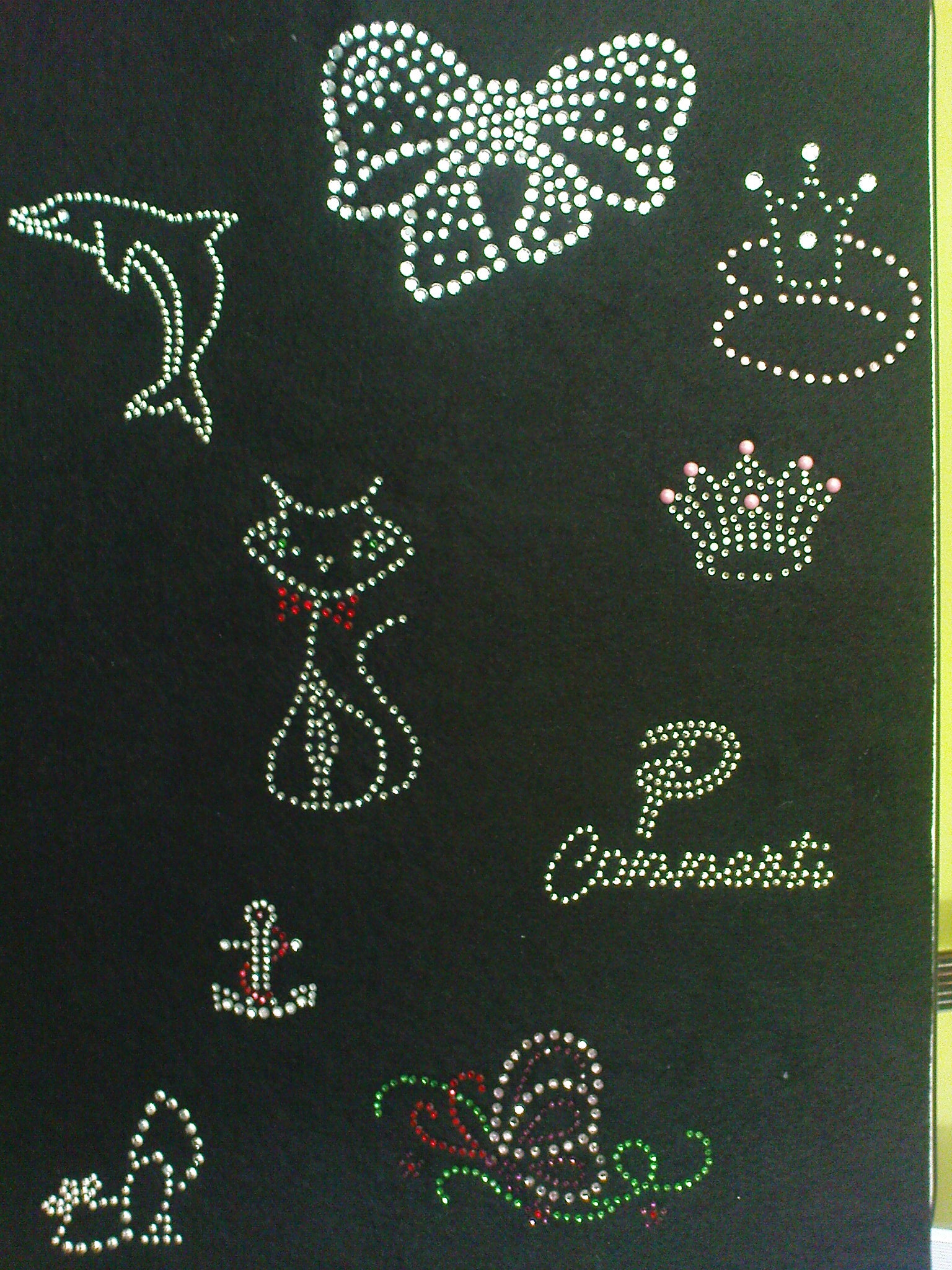 Czarna tkanina z aplikacjami z dżetów i kamieni ozdobnych w kształcie delfina, kokardy, dwóch koron, kota z czerwoną muszką, napisu 'Comonata' oraz kotwicy z czerwonymi akcentami i abstrakcyjnego...