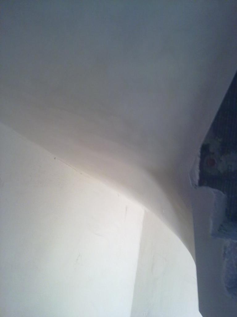 Świeżo otynkowana ściana i sufit w rogu pomieszczenia, widoczne niedoskonałości wykończenia przy krawędzi kolumny.