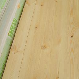 Centrum Drewna Profilowanego i Budowlanego - Jasne deski podłogowe z widocznymi sękami, ułożone pionowo, z fragmentem opakowania z logo producenta widocznym po lewej stronie.